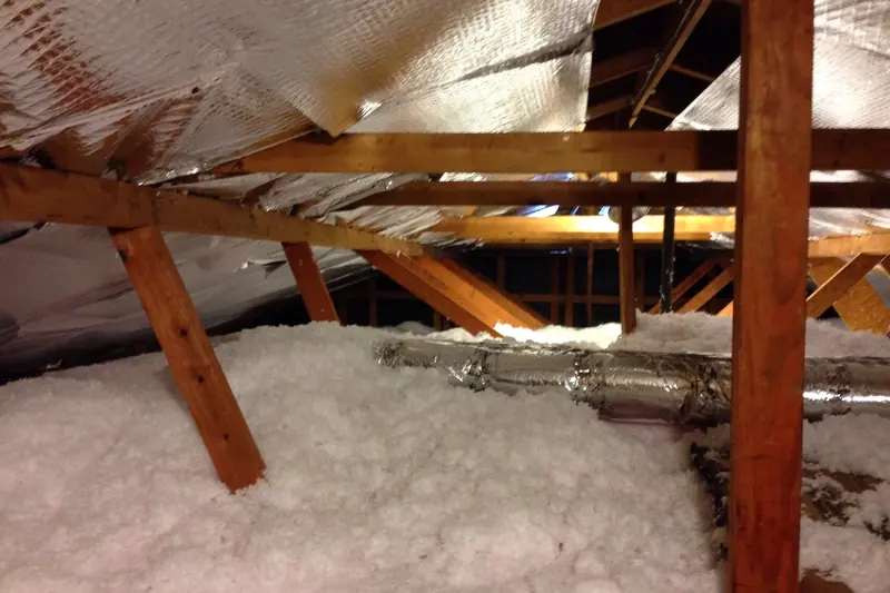 Photo of a foil-faced flexible duct stretched across a deep layer of blown-in attic insulation
