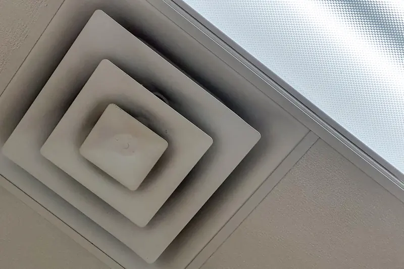 Square ceiling diffuser with streaks of gray dust darkening its louvers