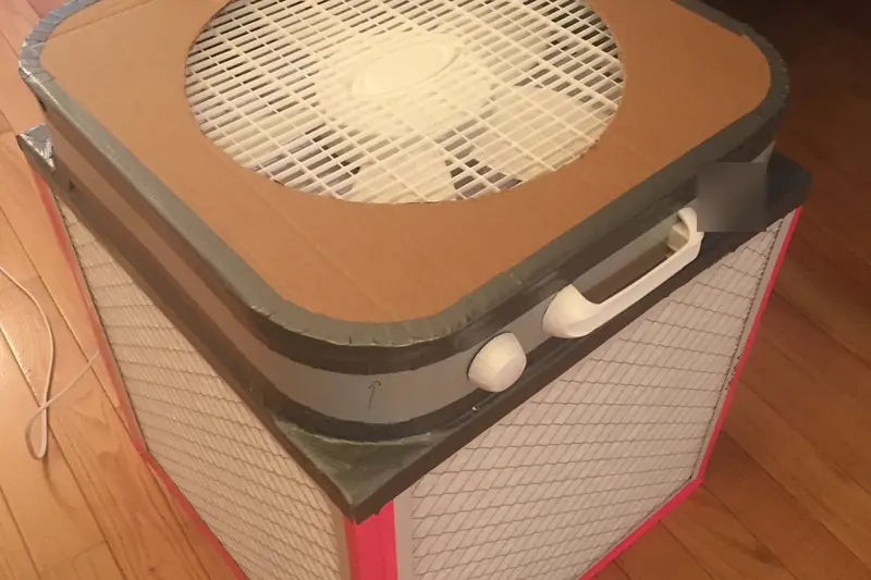 Home-built air cleaner made from a box fan with white pleated filters taped around its sides