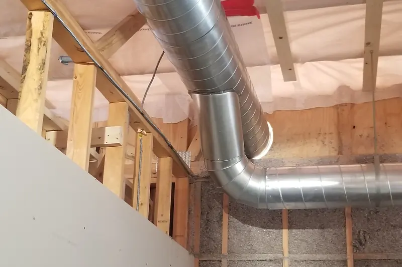 Bare galvanized spiral ducts and one elbow hanging beneath exposed wood ceiling framing